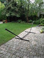 Full view of the black metal hammock stand placed on a paved patio with green grass and trees in the background.
