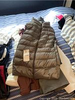 Brown sleeveless puffer vest on bed with tag marked '2 jackets'.