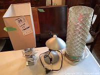 Three lamps on a table, tall white lamp with rectangular shade, silver small lamp, and tall textured glass mirrored lamp.