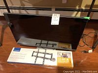 Dell 28-inch monitor and Insignia TV wall mount box placed on the floor, showing front view of monitor and full box graphics of wall mount.