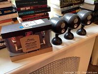 View of three black motion sensor lights and boxed door knob on white surface with books in background
