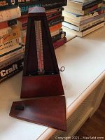 Wooden German metronome with pendulum, placed next to books on a white surface.
