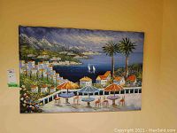 Full view of original coastal landscape painting depicting terrace with umbrella tables, palm trees, houses, ocean and mountains.