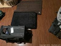 Three pet accessories placed on wood floor: soft carrier, black cushion, brown cushion.