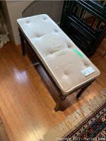 Piano bench top view showing padded beige tufted upholstery.