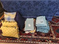 Pillows, pillow covers, and folded light blue velveteen drapes on a patterned carpet.