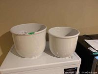 Two white plant pots placed on a white surface, the largest measuring 15x13 inches.