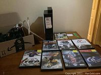 Photo showing the PS2 console, two controllers, seven game cases lined up, and an open box with cables inside.