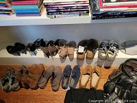 Wide view of 14 pairs of ladies footwear arranged in two rows on wooden floor and white shelving including boots, casual shoes, flats mostly size 9