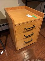 Front view of wooden side table showing three drawers with black handles and raised edges on top.