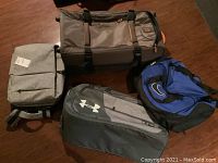 Four soft bags arranged on a wooden floor showing Timberland suitcase, Nike gym bag, Hansen and Modernist backpacks.