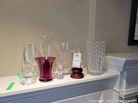 Assorted six glass vases displayed on a shelf with a label on one vase.