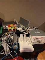 Full view of Nintendo Wii console, Wii remotes, cables, game cases, and other assorted items on a table.