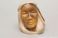 Front view of the soapstone carving showing the carved female face with a smooth brown finish and textured light hair.