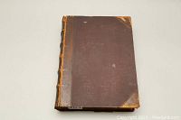 Front cover of large brown leather hardcover book with worn edges and corner scuffs.