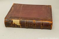 Photo showing the full book closed with worn brown leather cover and damaged spine with missing piece.