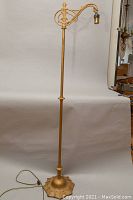 Full view of gold-tone cast metal floor lamp with a single light socket and bridge arm design.