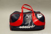 Front view of Adidas navy blue vinyl gym duffle bag with red vinyl handles and accents, showing Adidas trefoil logo in white on bottom right corner.