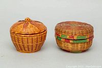 Pair of small indigenous handmade covered woven wicker bowls shown from front angle on white background.