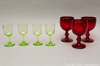 Four lime green monogrammed glass goblets and three ruby red glass goblets shown from front angle on neutral background.
