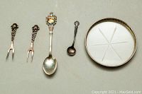 Four sterling silver cutlery pieces and one glass coaster with a sterling silver rim laid flat on a gray surface