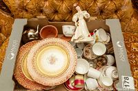 Top view of assorted chinaware including plates with floral patterns, several teacups and saucers, small metal teapot and porcelain figurine.