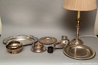 Photo showing single lamp with lampshade and all silver plated trays and serving pieces arranged on a table.