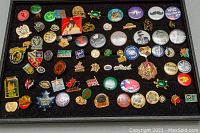 Photo of assorted vintage pins laid out on black background showing variety of pins including Toronto Maple Leaf, USA flag, St Johns Ambulance, novelty pins and others.