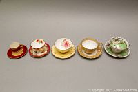 Front view of five vintage demitasse teacup and saucer sets showing varied colors and floral patterns