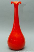 Front view of the tall orange glass vase with flared and ruffled rim, showcasing smooth vibrant color and glossy finish.