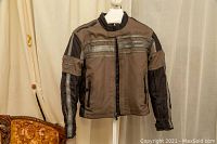 Full front view of the brown and black textile motorcycle jacket on a mannequin, showing zippered pockets, reflective stripes, and stand collar.