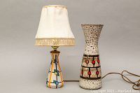 Photo showing lamp with fabric shade and ceramic vase side by side on a neutral background with cords visible.