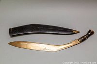 Full view of kukri sword placed next to its wooden sheath with metal tip, showing overall length and design.
