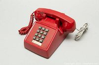 Front angle of red vintage Northern Telecom push button phone showing keypad and coiled cord.