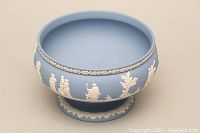 Front view of light blue Wedgwood jasperware pedestal bowl with white relief classical figures and leaf garland around body.