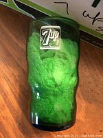 Close-up of a single green 7up glass tumbler showing the retro 7up logo design in white and the shape of the glass.