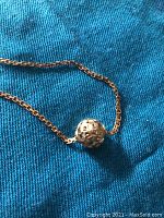 Close-up image of the textured hollow gold orb sliding on the rectangular link chain, highlighting its geometric facets and polished finish.