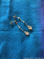 Pair of 14K gold dangle earrings displayed on blue fabric, showing chain design with small ball accents and round bottom charm.