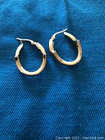 Both earrings laid face-up on blue fabric background