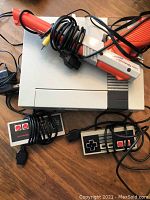 Nintendo Entertainment System console with two controllers and Zapper on wooden floor with cables visible