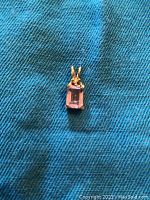 Top view of a rectangular amethyst pendant in 10KT gold with purple gemstone and gold bail.