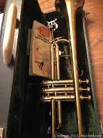 Closed up view of the trumpet inside its green velvet-lined case, showing the brass finish and included care instructions booklet.