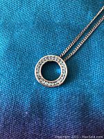 Close-up of circular silver pendant with light blue stones around edge on blue fabric.