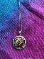 Close-up of the round gold pendant charm with Tree of Life design and the words Faith, Friends, Family, showing the three small diamonds on the charm.
