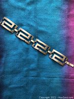 Silver geometric cut-out cuff bracelet laid flat showing the overall length and link design on blue and purple fabric.