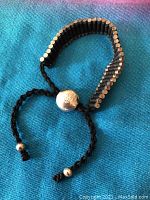 Photo showing the black braided cord bracelet with silver cylindrical beads and round silver adjustable clasp marked 'LINKS 925'