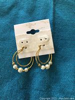 Front view of gold-tone double hoop earrings with three faux pearls on each earring, attached to white display card.