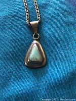 Close-up image of sterling silver necklace with triangular turquoise stone pendant on a blue fabric background.