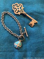 Photo showing sterling silver key pendant and silver toggle bracelet with turquoise heart charm on blue fabric