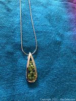 Close-up image of the silver necklace pendant showing three green gemstones set vertically in a teardrop shape.